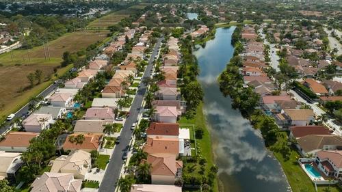 An aerial view high over a reflective pond, surrounded by beautiful houses in a residential neighborhood on a sunny day in Margate, Florida.