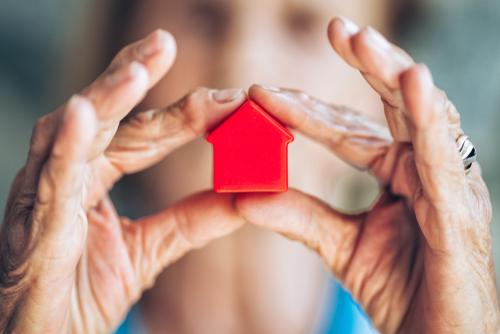 Elderly woman holding a small red house-shaped figurine between their hands